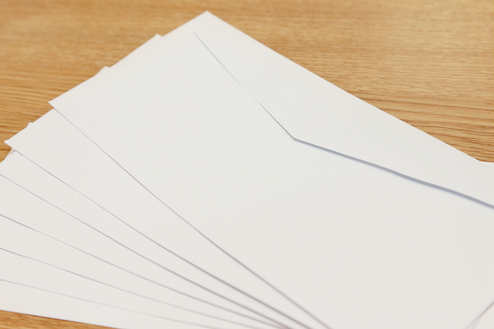 Stapel weißer Umschläge auf einer Holzoberfläche. Angeschnittene Ecken sind sichtbar.